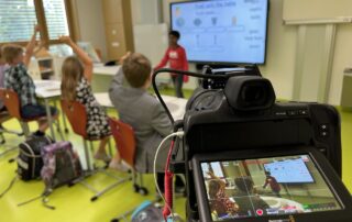 Kamera mit Display filmt Schulkinder vor dem Whiteboard – Dreh für die Stiftung Bildungspakt Bayern