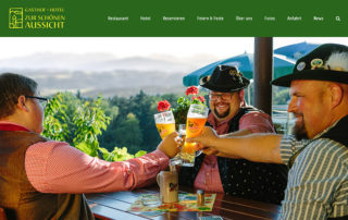 Website des Landgasthofs „Zur schönen Aussicht“: drei Männer in Tracht stoßen im Biergarten mit Weißbier an