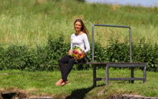 Barbara Hedtstück mit Blumenstrauß auf einer Bank in der Wiese – Fotoshooting für ihre neue Website