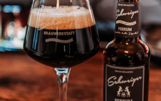 Glas und Flasche Schweiger FERRUM auf einem Holztisch – Verkostung des neuen Bieres