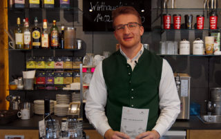 Juniorchef Maxi Hirschmann in Trachtenweste hinter der Bar der Königslinde am Tegernsee – „Bier ist der neue Kaffee“