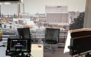 Interview-Set mit zwei Stühlen vor historischem Foto des Pfanni-Werks, davor ein Monitor – Dreh „Pfanni Persönlichkeiten“