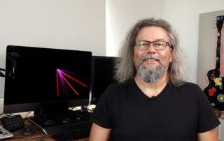 Michael J. Müller spricht vor Monitor und Gitarre in die Kamera – Tutorialfilm zum Videopodcast Schindhelm 365
